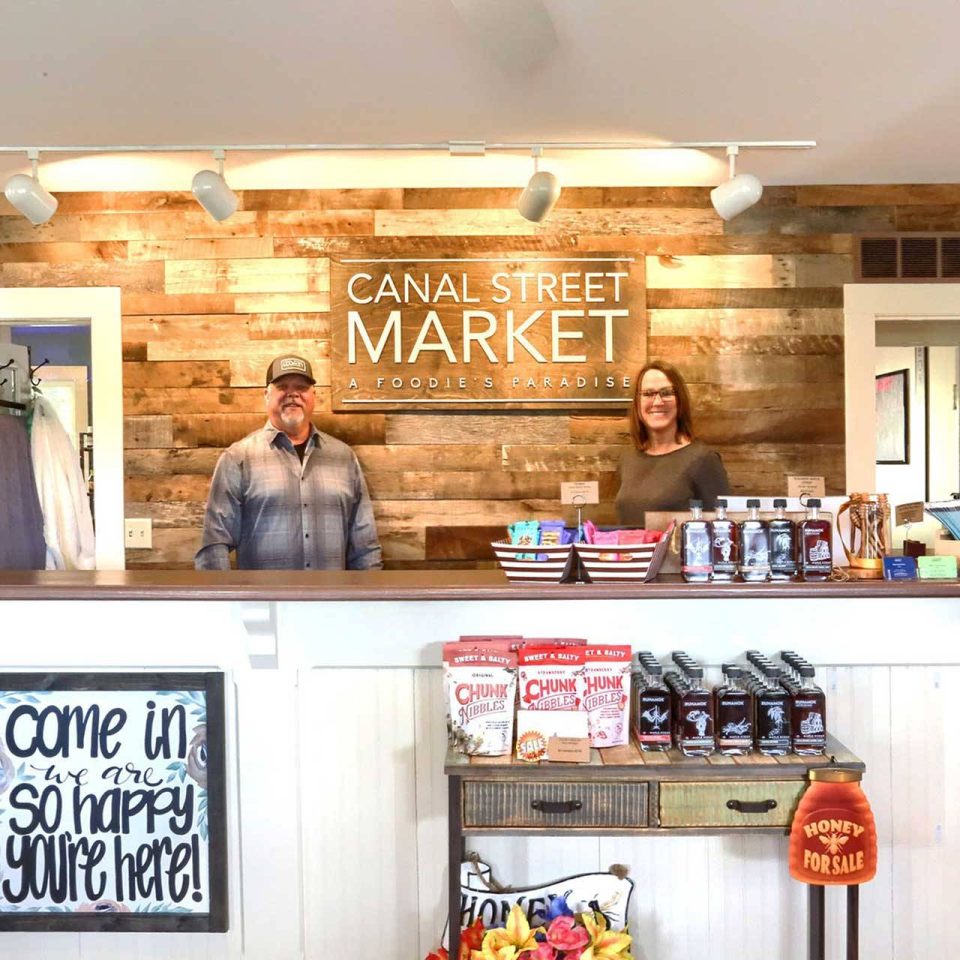 Interior Canal Street Market sign with Billy and Maria Hutchinson standing next to it behind the front counter.