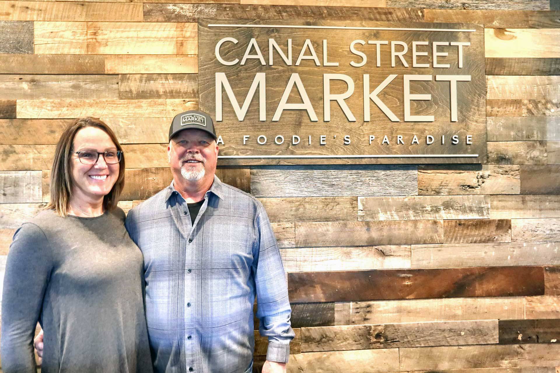 Interior Canal Street Market sign with Billy and Maria Hutchinson standing next to it.